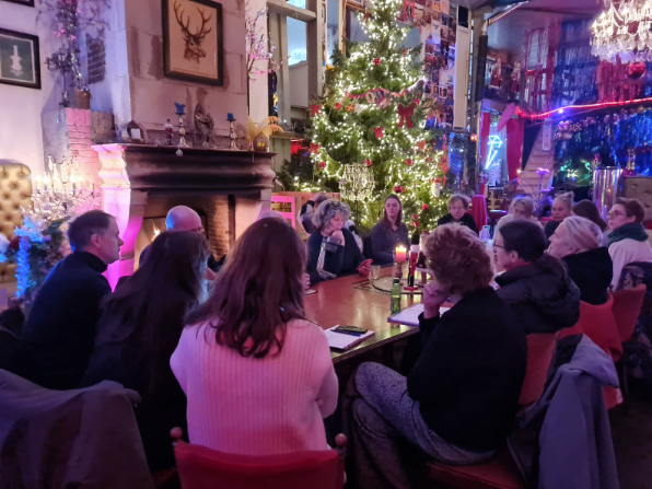 Veertien mensen aan een tafel in een ruimte met kerstversiering en een kerstboom