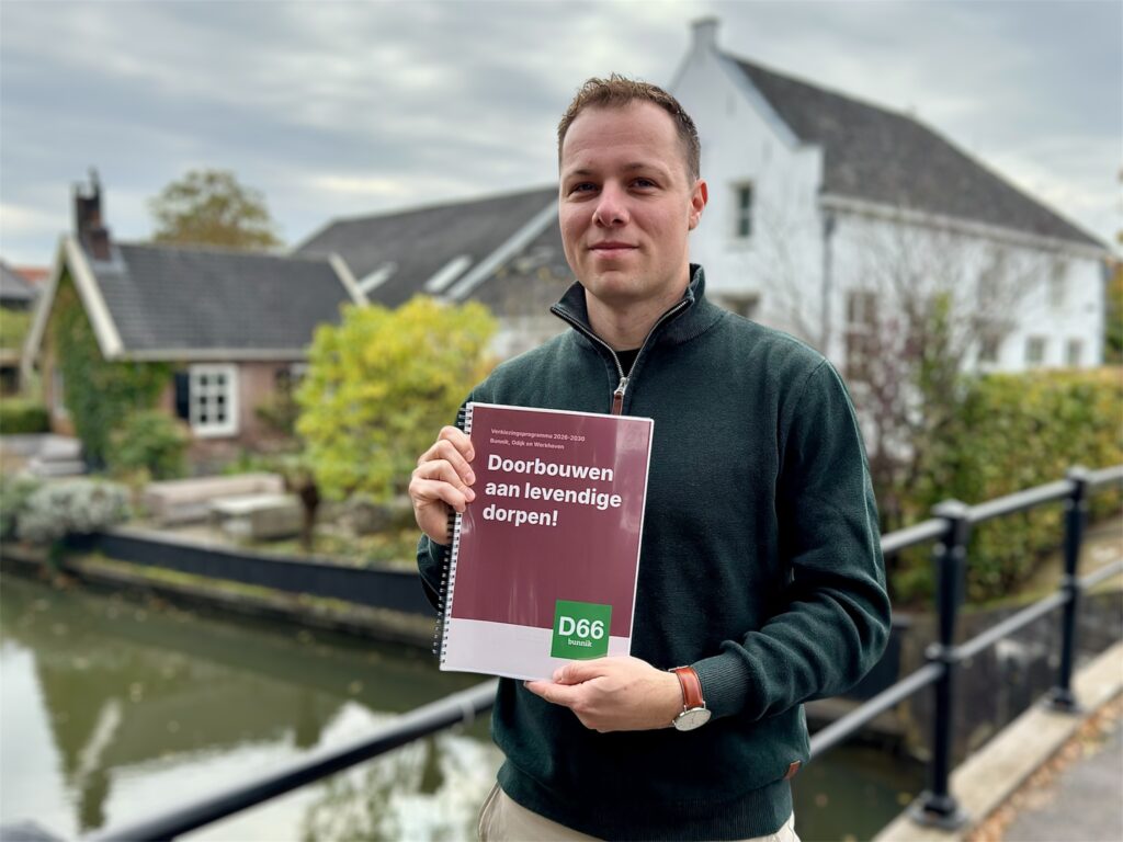 Onno James houdt het verkiezingsprogramma 2026-2030 "Doorbouwen aan levendige dorpen!" vast, staand op de raadhuisbrug met een wit huis op de achtergrond