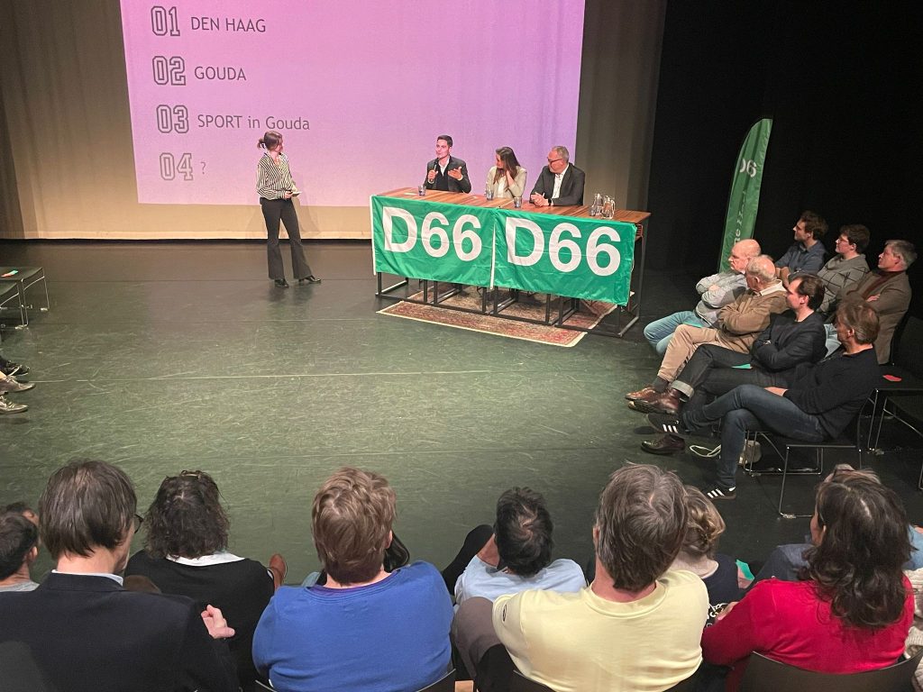 Een foto waarin het panel met Rob Jetten, Jitske Flietstra en Frank Berteling vanuit de zaal te zien zijn.