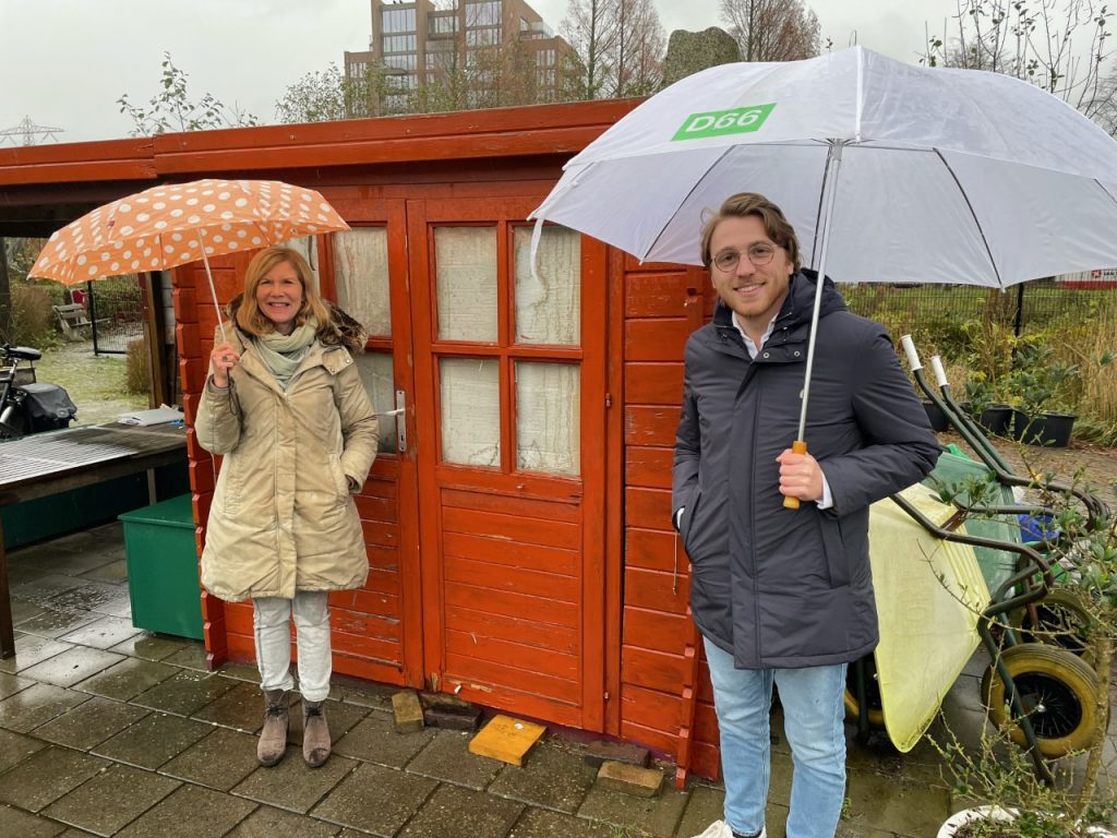 Charlotte en Wouter staan met paraplu voor een tuinhuisje bij amateur tuinvereniging Nicolaas Beets